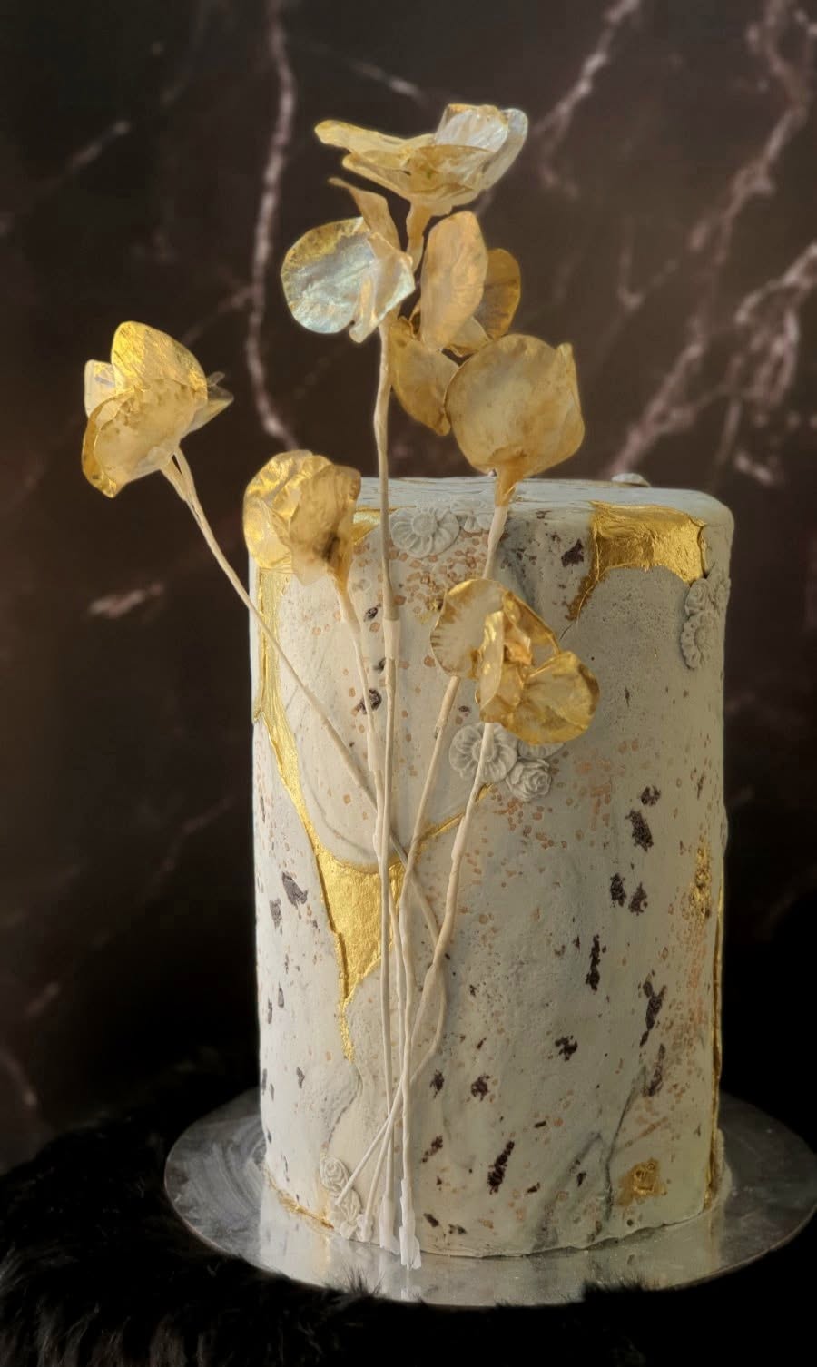 A textured cake finished with gold-leaf sugar flowers by 21Treats