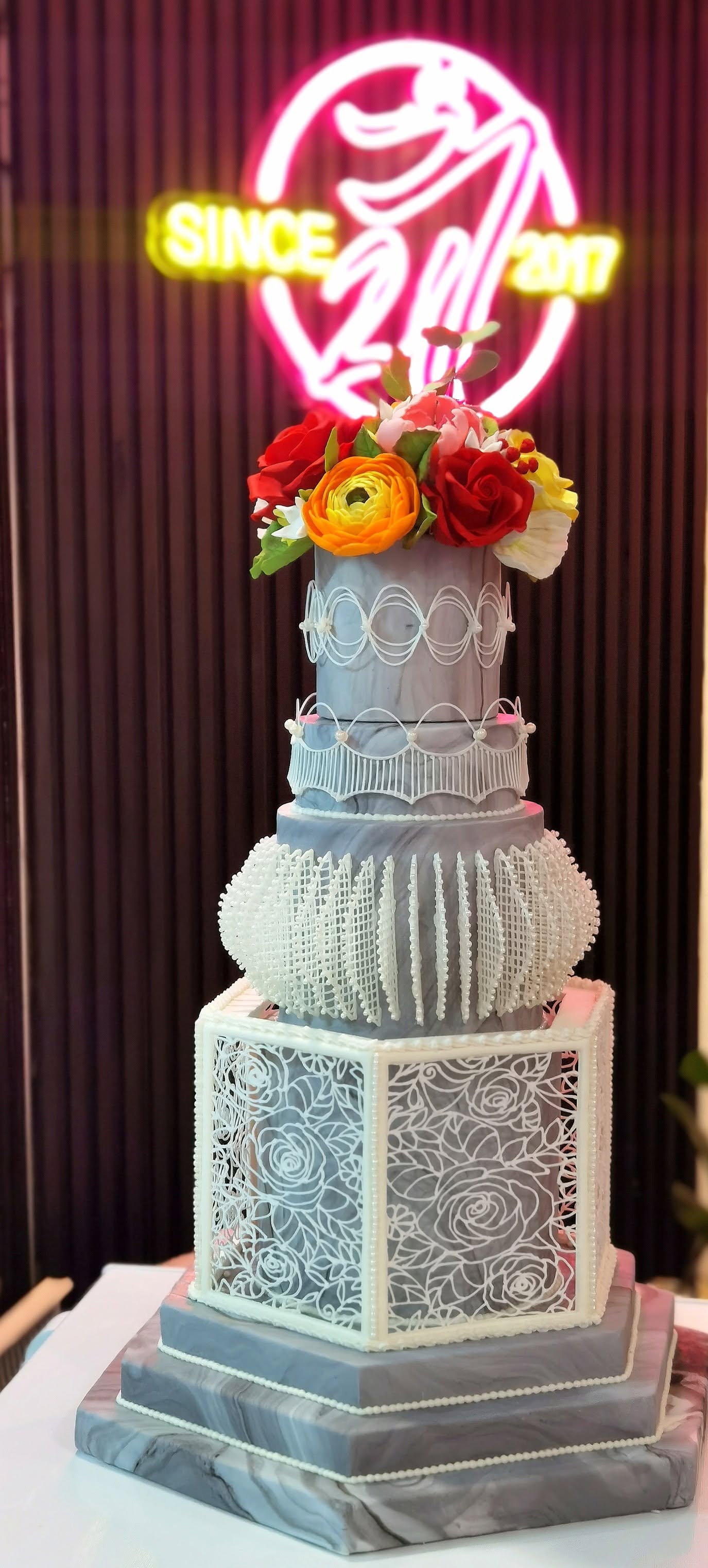 A grand 21Treats wedding cake in front of the bakery's 'Since 2017' neon sign